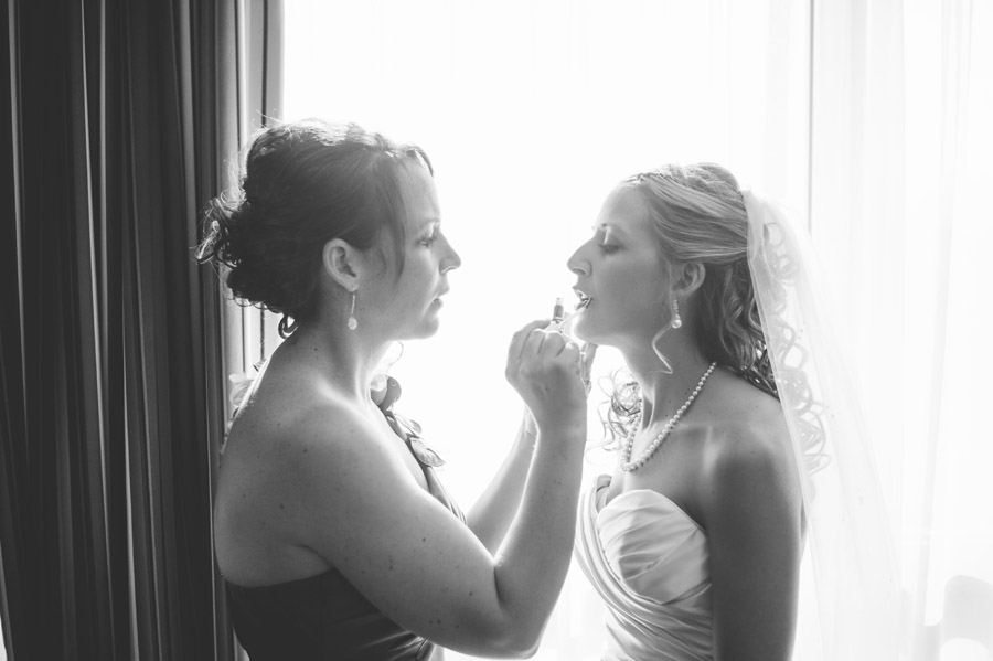 maid of honor helps bride finish makeup before wedding