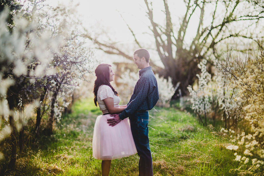 Bride in pink tutu poses in apple blossom field in Longmont for engagement photos